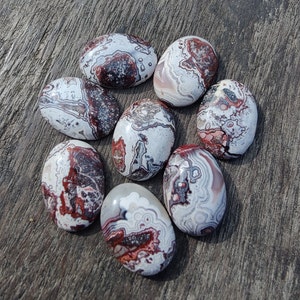 May include: Seven oval-shaped agate stones with a white, grey, and red swirling pattern. The stones are smooth and polished.