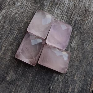 Peut inclure: Quatre pierres précieuses en quartz rose rectangulaires et facettées. Les pierres sont d'un rose tendre et ont une taille géométrique. Elles sont disposées sur une surface en bois gris vieilli.