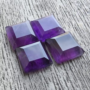 May include: Four square-cut, faceted amethyst gemstones arranged on a weathered wooden surface. The gems display a deep purple hue with reflective facets, showcasing their clarity and cut. The arrangement suggests a focus on jewelry or gemstone crafts.