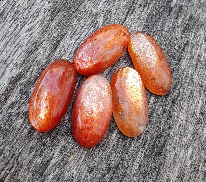 K&ouml;nnte beinhalten: F&uuml;nf ovale Sonnen&shy;steine mit schimmerndem, irisierendem Finish. Die Steine sind in Orange- und Rott&ouml;nen gehalten.
