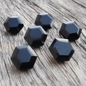 May include: Six black, faceted, hexagonal buttons on a wood surface.