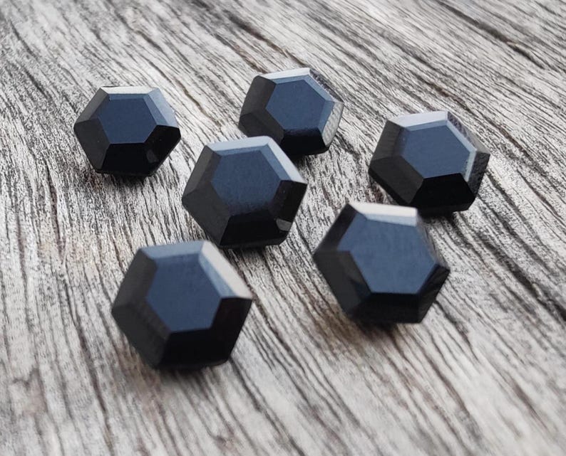 May include: Six black, faceted, hexagonal buttons on a wood surface.
