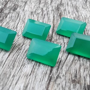 May include: Five green gemstone cabochons in a rectangular shape, with beveled edges, on a wooden surface.