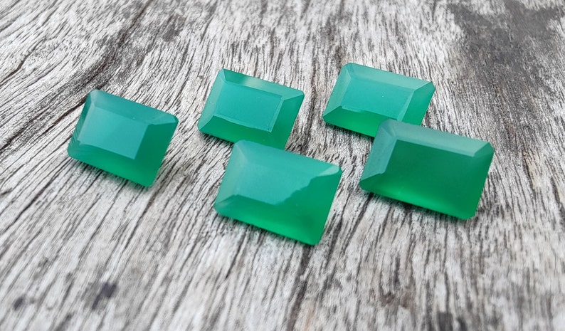 May include: Five green gemstone cabochons in a rectangular shape, with beveled edges, on a wooden surface.