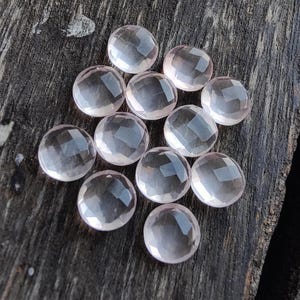 May include: A collection of twelve faceted rose quartz stones, each with a smooth, rounded surface. The stones are a pale pink color and have a translucent appearance.