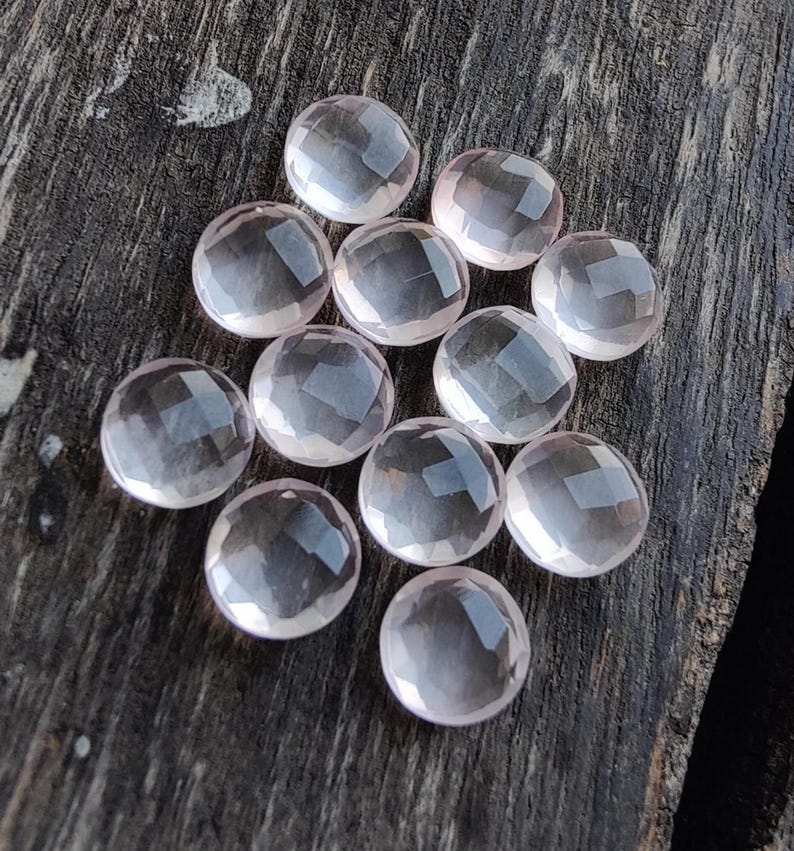 May include: A collection of twelve faceted rose quartz stones, each with a smooth, rounded surface. The stones are a pale pink color and have a translucent appearance.