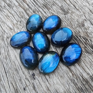 May include: Eight oval-shaped labradorite gemstones in shades of blue and grey. The stones are smooth and polished, with a slight iridescent sheen.
