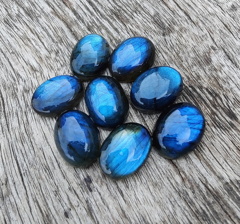 May include: Eight oval-shaped labradorite gemstones in shades of blue and grey. The stones are smooth and polished, with a slight iridescent sheen.