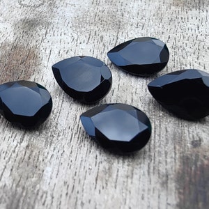 May include: Five black teardrop-shaped gemstones on a wooden surface.