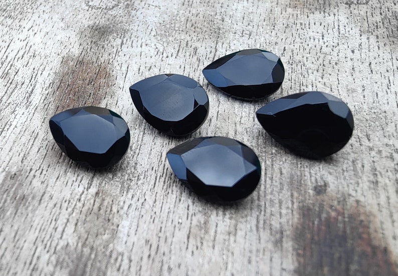 May include: Five black teardrop-shaped gemstones on a wooden surface.