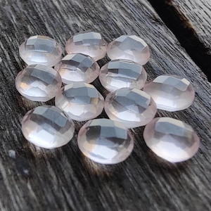 May include: A collection of 12 faceted rose quartz stones, each with a light pink hue and a translucent appearance. The stones are arranged in a loose cluster on a wooden surface.