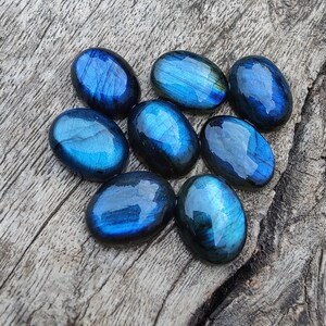 May include: Eight oval-shaped labradorite gemstones in shades of blue and green. The stones are smooth and polished, with a iridescent sheen.