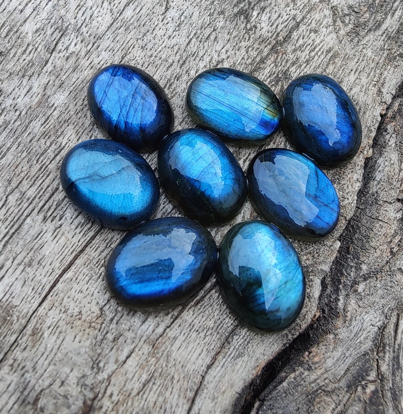 May include: Eight oval-shaped labradorite gemstones in shades of blue and green. The stones are smooth and polished, with a iridescent sheen.
