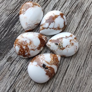 Puede incluir: Cinco piedras de cabuj&oacute;n blancas con vetas marrones y negras. Las piedras tienen forma de l&aacute;grima y un acabado liso y pulido.