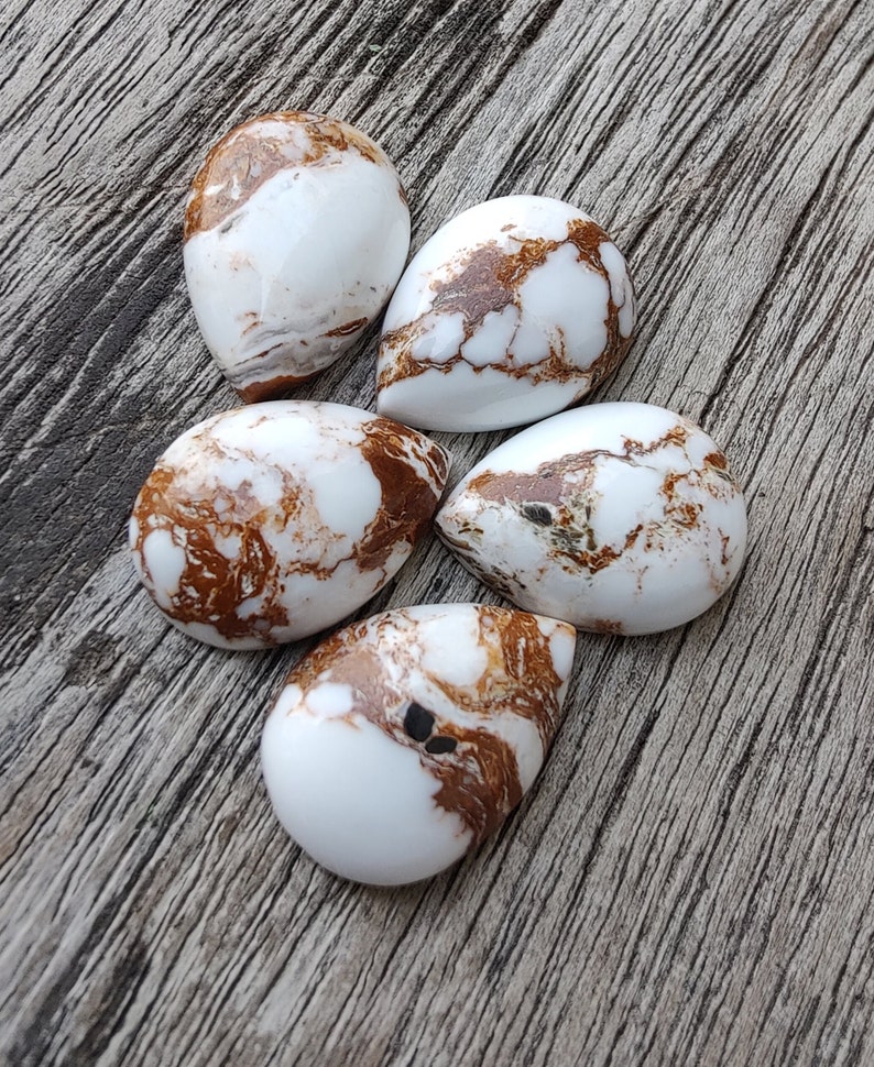 Puede incluir: Cinco piedras de cabuj&oacute;n blancas con vetas marrones y negras. Las piedras tienen forma de l&aacute;grima y un acabado liso y pulido.