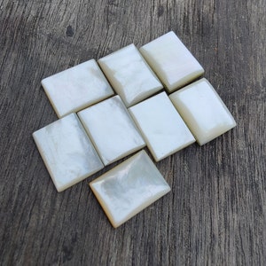 Può includere: Otto piastrelle rettangolari bianche iridescenti disposte a spina di pesce su una superficie di legno.