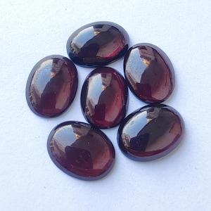 Puede incluir: Seis piedras preciosas ovaladas de color rojo oscuro con un acabado brillante. Las piedras preciosas est&aacute;n dispuestas en un c&iacute;rculo sobre un fondo blanco.