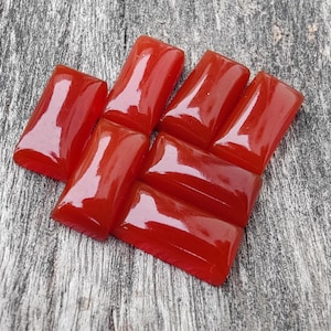 Könnte beinhalten: Eine Gruppe von acht roten Karneol-Cabochons, in rechteckiger Form geschnitten, die in einem Muster auf einer Holzoberfläche angeordnet sind.