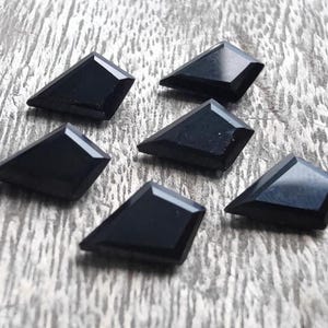 May include: Six black diamond-shaped gemstones on a wooden background.