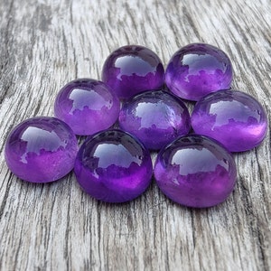 May include: Eight smooth, round, purple amethyst stones on a wooden surface.