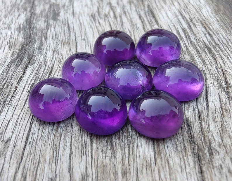 May include: Eight smooth, round, purple amethyst stones on a wooden surface.