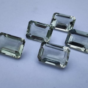 Può includere: Cinque pietre preziose verdi a taglio smeraldo su uno sfondo bianco.