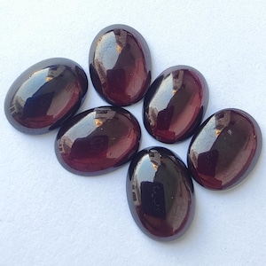 Puede incluir: Seis piedras preciosas de forma ovalada con un color rojo oscuro y negro. Las piedras preciosas tienen una superficie lisa y pulida y est&aacute;n dispuestas en semic&iacute;rculo.
