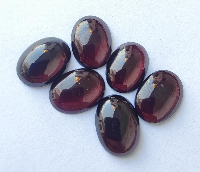 Puede incluir: Seis piedras preciosas de forma ovalada con un color rojo oscuro y negro. Las piedras preciosas tienen una superficie lisa y pulida y est&aacute;n dispuestas en semic&iacute;rculo.