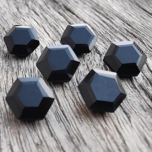 May include: Six black, faceted, hexagonal buttons on a wooden surface.