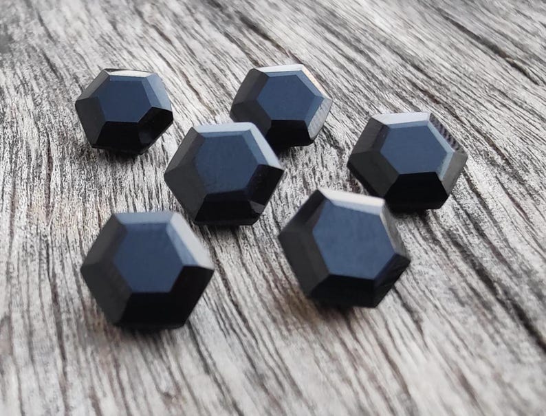 May include: Six black, faceted, hexagonal buttons on a wooden surface.