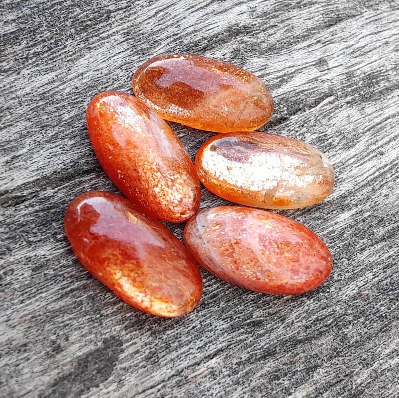 K&ouml;nnte beinhalten: F&uuml;nf glatte, ovalf&ouml;rmige Sunstone-Steine in Orange- und Goldt&ouml;nen. Die Steine haben eine schimmernde, irisierende Qualit&auml;t.