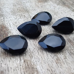 May include: Five black teardrop-shaped faceted gemstones on a wooden surface.