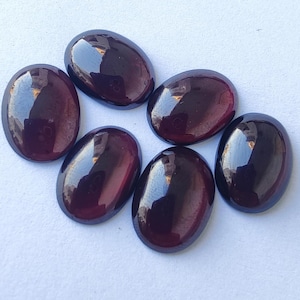 Puede incluir: Seis piedras preciosas ovaladas de color p&uacute;rpura oscuro. Las piedras tienen una superficie lisa y pulida y un ligero brillo iridiscente.