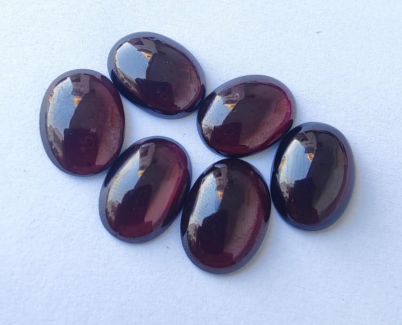 Puede incluir: Seis piedras preciosas ovaladas de color p&uacute;rpura oscuro. Las piedras tienen una superficie lisa y pulida y un ligero brillo iridiscente.