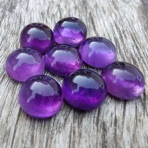 May include: Eight round, purple amethyst stones on a wooden surface.