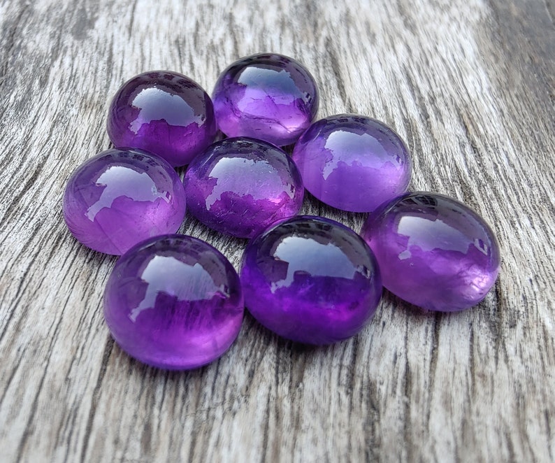 May include: Eight round, purple amethyst stones on a wooden surface.