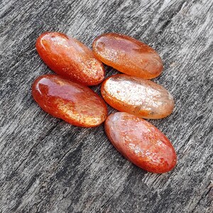 K&ouml;nnte beinhalten: F&uuml;nf ovale Sunstone-Steine mit schimmerndem, irisierendem Finish. Die Steine sind eine Mischung aus Orange und Rot mit einem metallischen Schimmer.