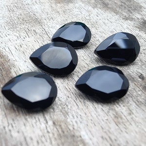 May include: Five black teardrop-shaped gemstones on a wooden surface.