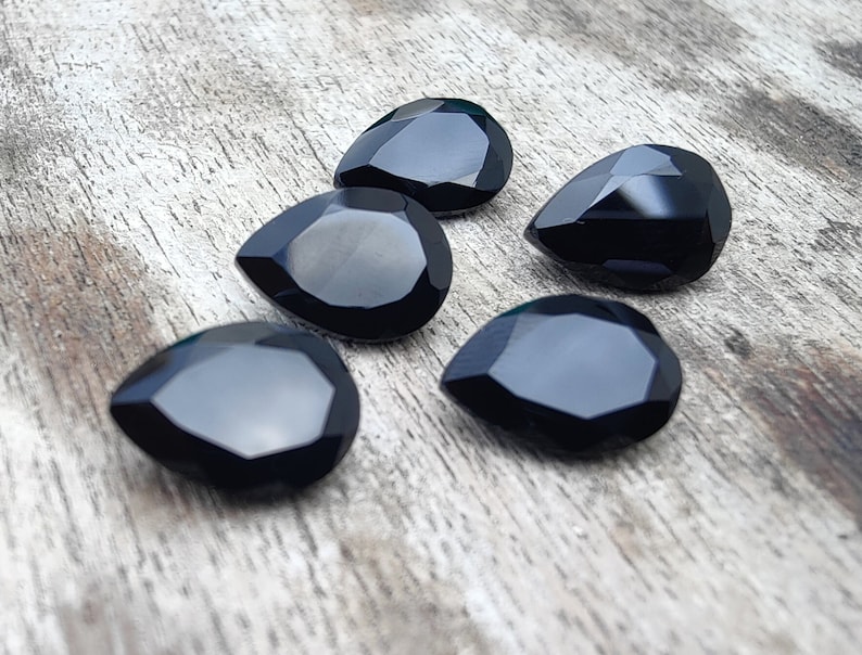 May include: Five black teardrop-shaped gemstones on a wooden surface.