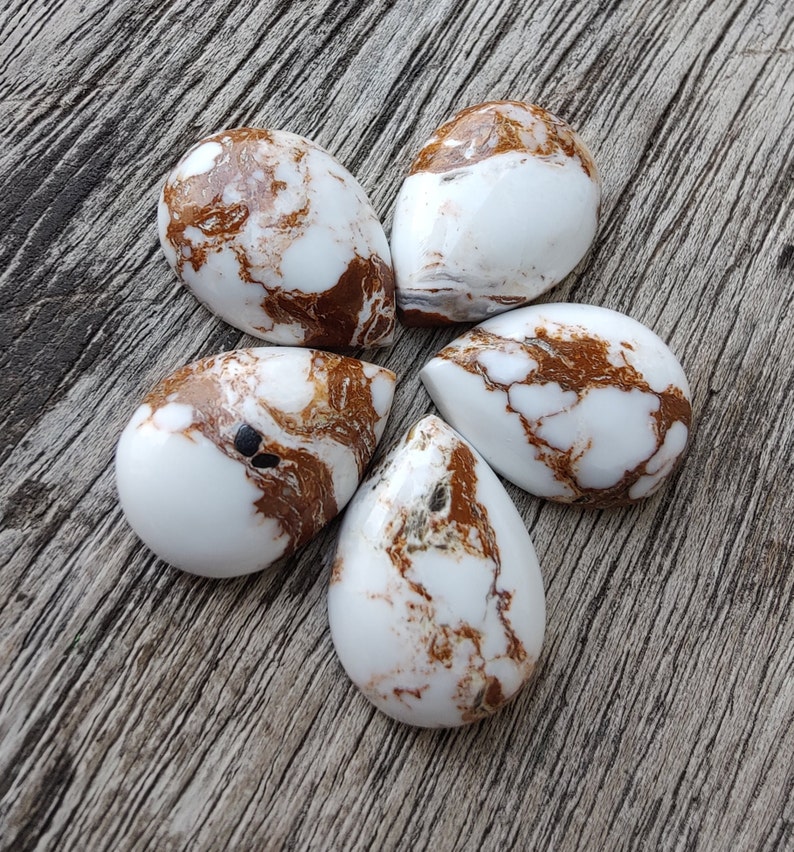 Puede incluir: Cinco cabujones en forma de l&aacute;grima de color blanco y marr&oacute;n con un patr&oacute;n de m&aacute;rmol. Los cabujones est&aacute;n dispuestos en forma de flor sobre una superficie de madera.