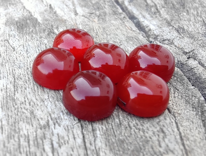 K&ouml;nnte beinhalten: Sechs runde, rote Cabochonsteine auf einer Holzoberfl&auml;che.