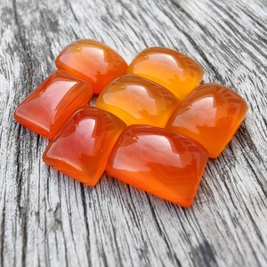 May include: A cluster of polished, orange gemstones with a glossy finish. The stones are various shapes, some rectangular and others rounded. The colour shifts from a deep red-orange to a bright, sunny orange.