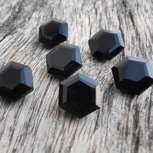 May include: Six black, faceted, hexagonal buttons on a wood background.