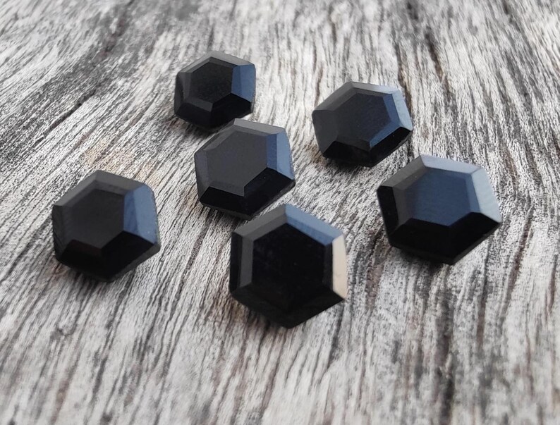 May include: Six black, faceted, hexagonal buttons on a wood background.