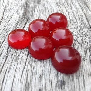 K&ouml;nnte beinhalten: Sieben glatte, runde, rote Edelstein-Cabochons auf einer grauen Holzoberfl&auml;che.