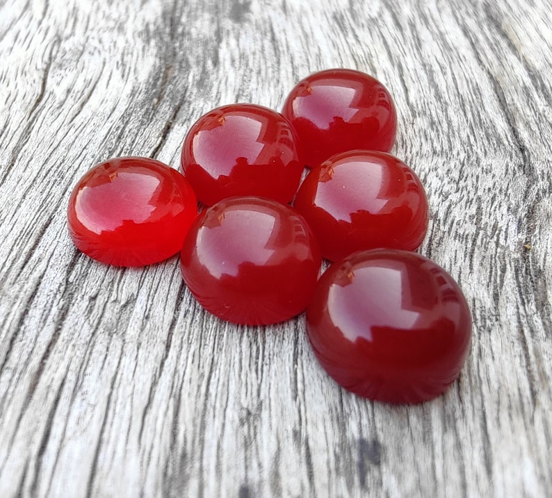 K&ouml;nnte beinhalten: Sieben glatte, runde, rote Edelstein-Cabochons auf einer grauen Holzoberfl&auml;che.