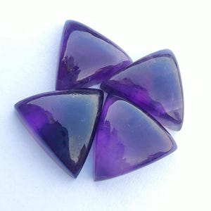 Puede incluir: Cuatro piedras preciosas de amatista triangulares, cada una con un tono púrpura y una superficie lisa y pulida.
