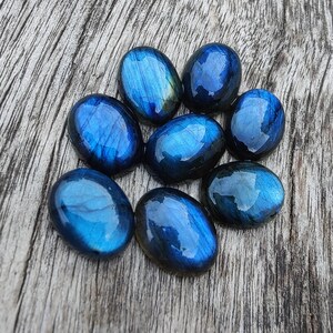 May include: Eight smooth, oval-shaped labradorite stones in shades of blue and grey. The stones are arranged in a circular pattern on a wooden surface.