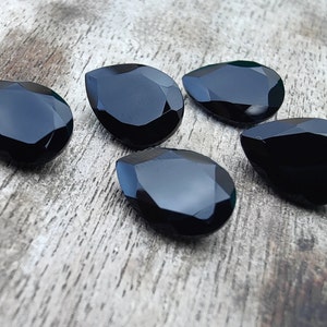 May include: Five black teardrop-shaped gemstones on a wooden surface.