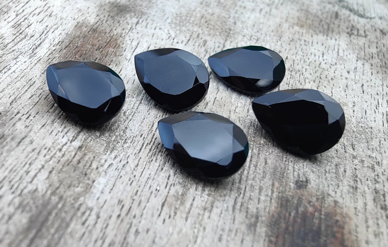 May include: Five black teardrop-shaped gemstones on a wooden surface.